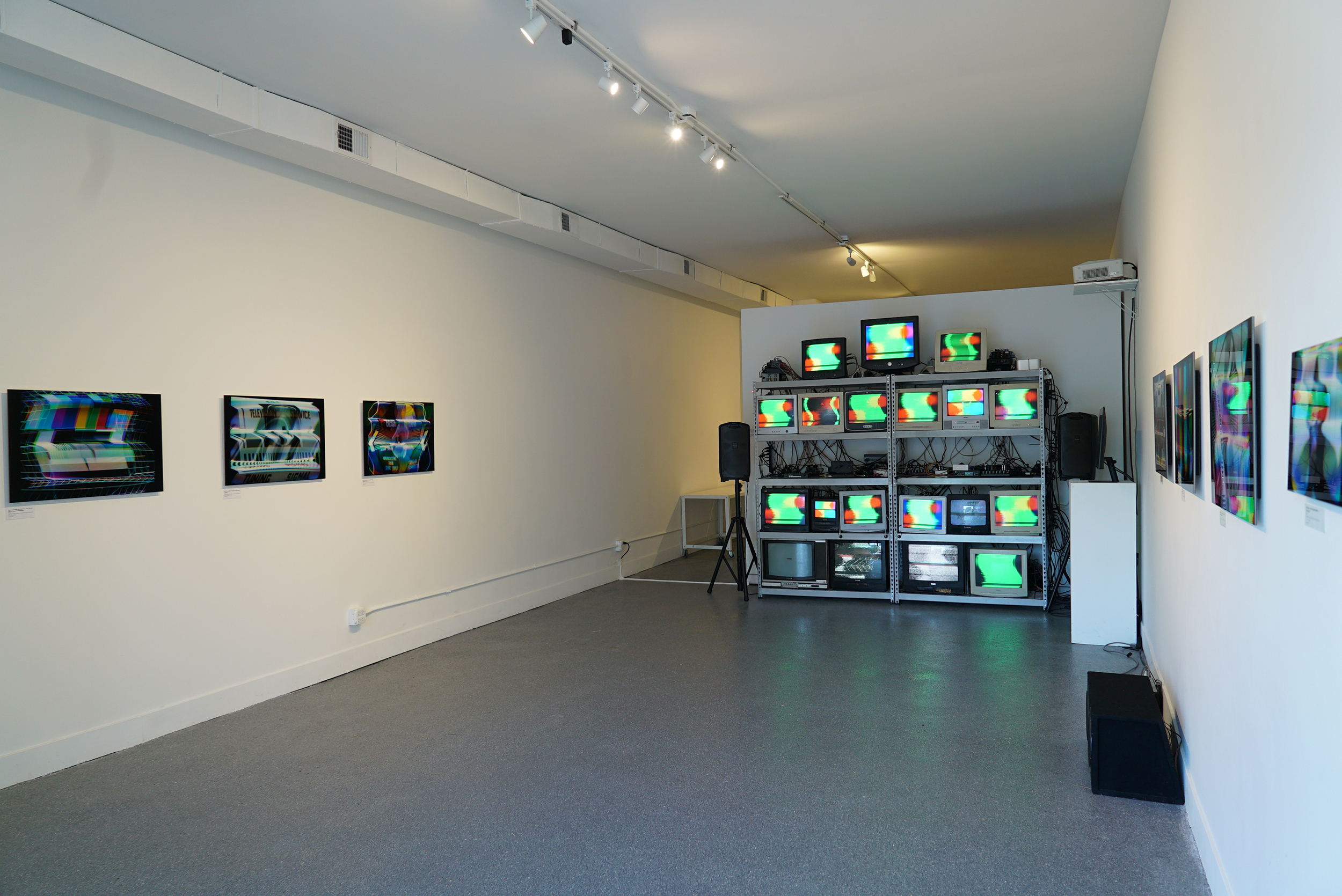 Wide shot of the 19 CRT television and computer monitor installation showing the installation in a gallery space with images hung on the walls.