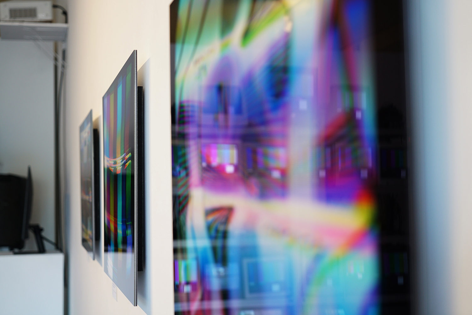 Face-mouted prints hanging on wall photographed at a sharp angle with a shallow depth of field.