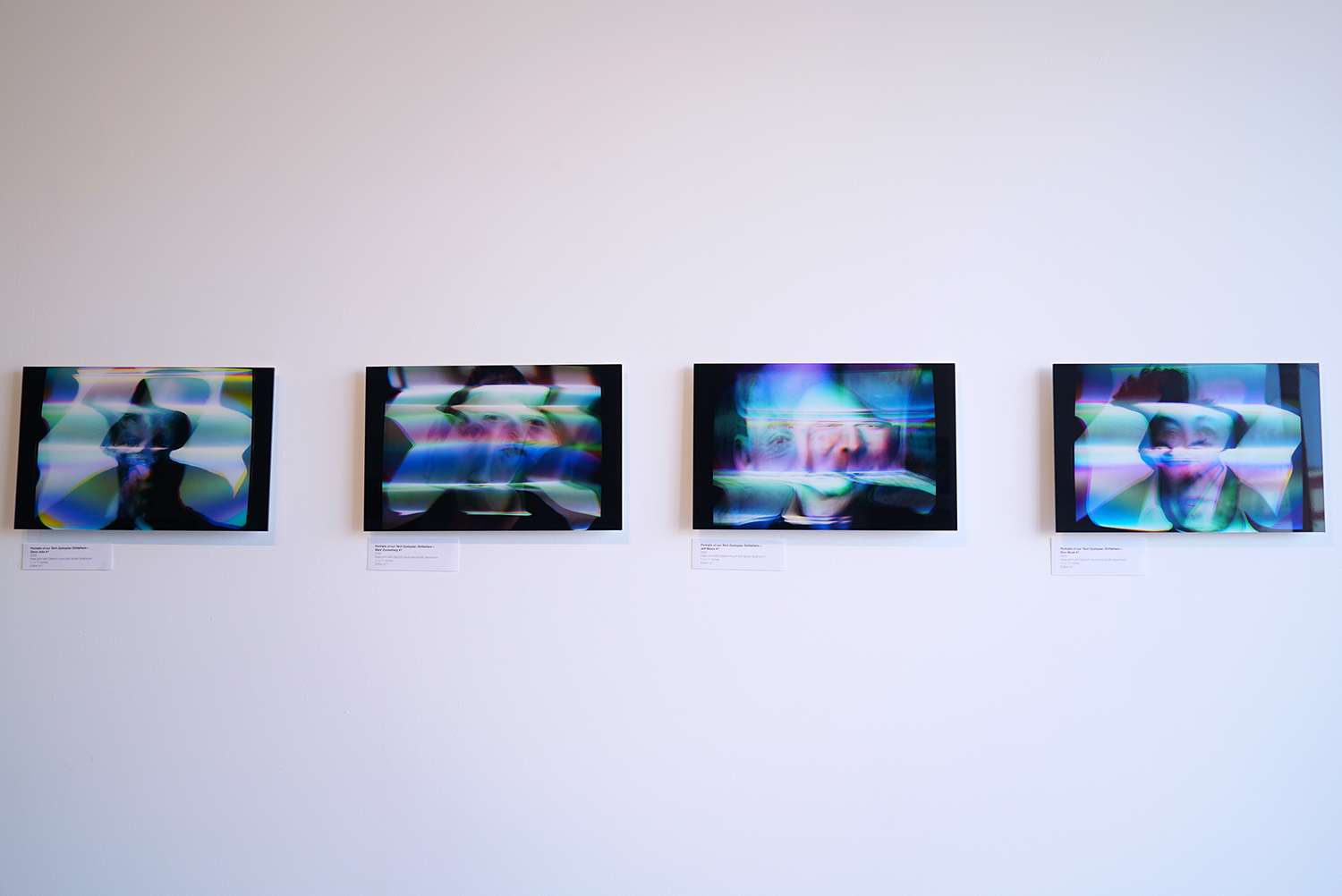 Face-mouted prints hanging on wall photographed at a sharp angle with a shallow depth of field.