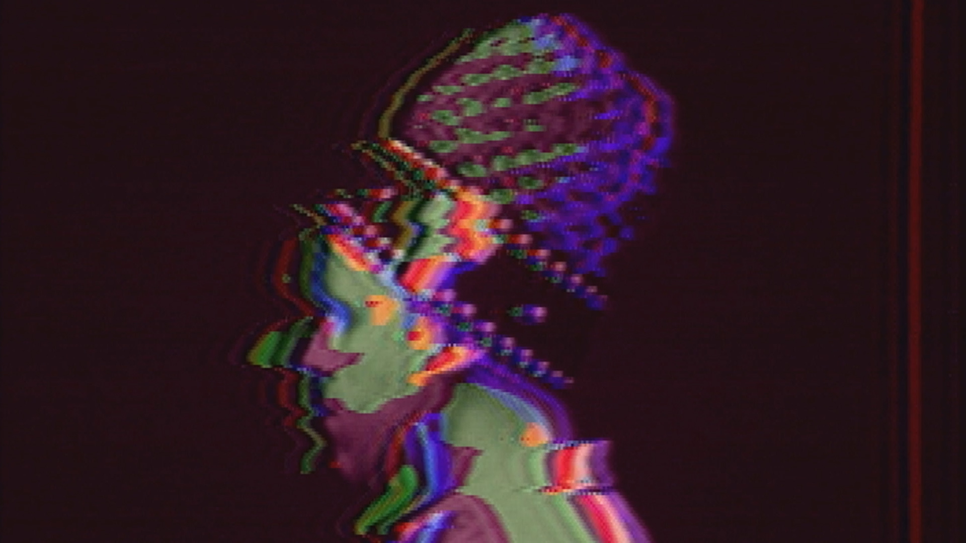 James Connolly from the shoulder's up facing the left wearing a recreation of Dan Sandin's hat tall hat from his 1973 'Romp Through the IP' video, processed on the Sandin Image Processor to have bright colors and broken imagery.
